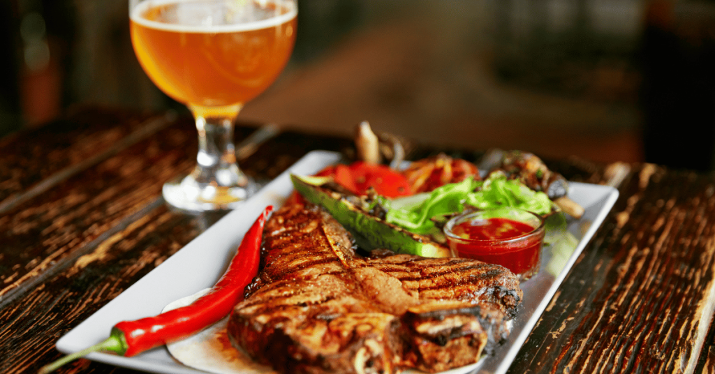 primo piano di piatto di carne con calice di birra sullo sfondo